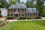 Well-maintained front yard with green lawn, trimmed hedges, and landscaped garden beds in front of a brick home in Elm Grove