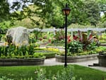 Well-maintained Milwaukee garden with colorful flower beds, trimmed hedges, and a decorative lamppost along a paved pathway.