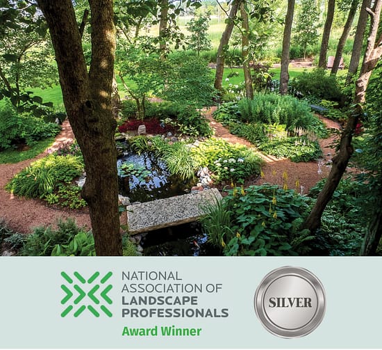 Shaded woodland garden with winding gravel paths, pond, and lush perennial plantings