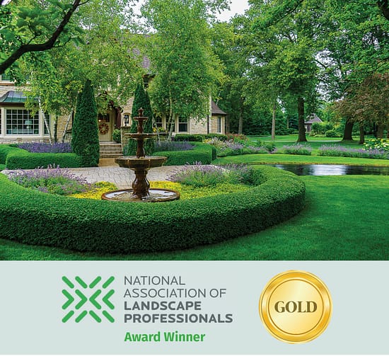 Formal residential landscape with circular hedge garden, stone fountain, and manicured lawn