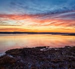 Sunset over a calm lake and wetlands with vibrant orange and blue sky, fine art landscape photography by David J. Frank.